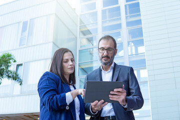 Businesswoman and businessman with tablet working in the street outside an office building