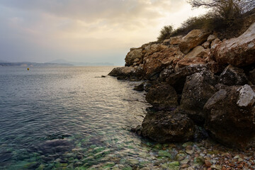 Stony beach next to the cliff rocks on a golden sunset.