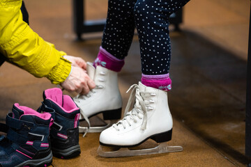 Woman is helping her daughter put her figure skates on before she takes her to a skating lesson.