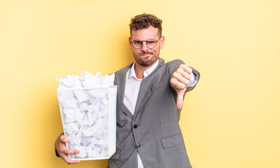 young handsome man feeling cross,showing thumbs down paper balls trash concept