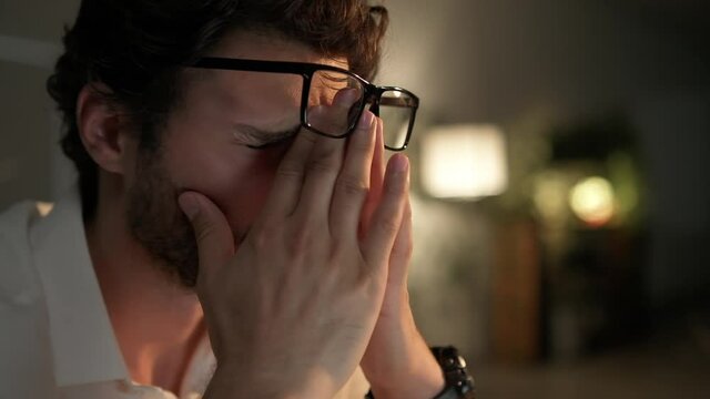 A side view of the man rubbing his eyes after work on laptop in the office at night