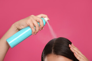 Young woman applying dry shampoo against pink background, closeup