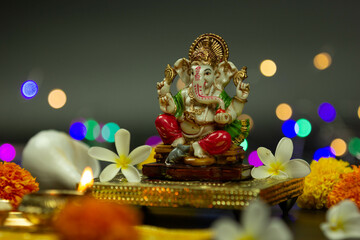 Side view of Statue Of Ganpati Bappa Hindu God Ganesha Sitting On Golden Asana With Fruits, Flowers, Lamp, shunkh And Blur Bokeh For Diwali New Year Deepawali Ganesh Chaturthi Or Shubh Deepavali Pooja