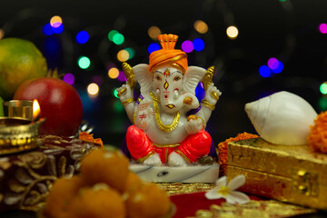 Moorti Murati of Ganpati Bappa Morya In Orange Pagdi For Worship On Diwali Puja New Year Deepawali Ganesh Chaturthi Or Shubh Deepavali Pooja. Laddu Sweet Ladoo And Shankh in Blur With Bokeh