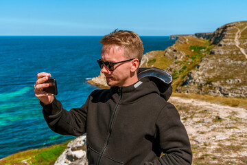 A young man takes pictures on his smartphone of a picturesque seascape with azure water on the western coast of Crimea.