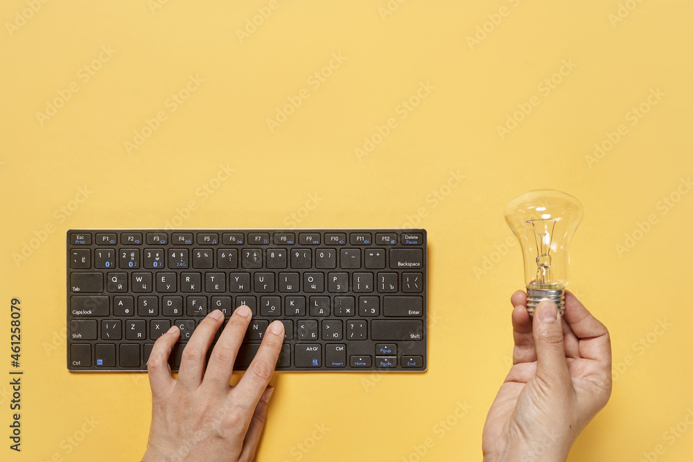 Poster top view of a person typing on the keyboard and holding a light bulb on a yellow surface