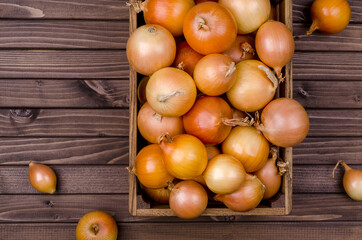 Large raw onions in a box on a wooden background.