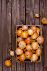 Large raw onions in a box on a wooden background.