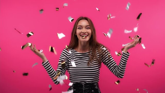excited woman throwing up sparkling confetti on pink