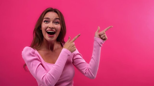 amazed and cheerful woman pointing away with fingers isolated on pink