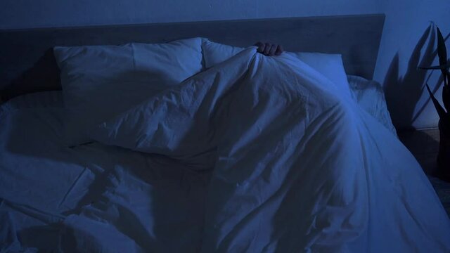 scared man hiding under blanket in bedroom with flashing light