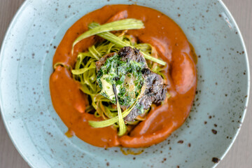 Grilled and flamed ox steak with green herb noodles in a tomato puree at a restaurant