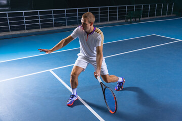 Full-length portrait of sportsman, professional tennis player serving a ball, training over indoor...