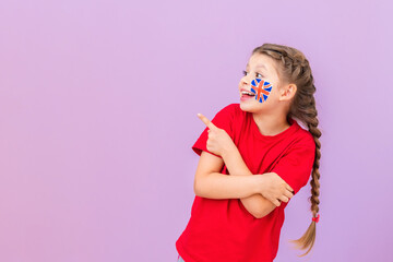 A student with a British flag painted on her cheek points her fingers to the side and smiles.
