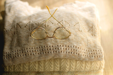 Pile of beige sweaters and retro eyeglasses. Selective focus.