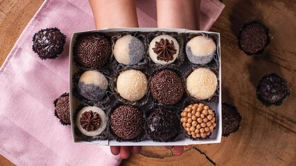 A child's hand holding a box with various types of gourmet brigadeiro. Typical sweet from Brazil. Brigadiers. Top view