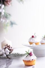 Fototapeta na wymiar Christmas cupcakes with vanilla frosting, cranberries and rosemary on white background. Vertical
