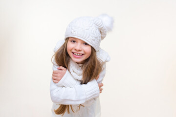 A girl in a white winter hat with a pompom and a warm winter sweater is happy and smiling. a child on an isolated background.