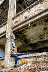 Teenage boy sitting on a crumbling building and using smarthphone
