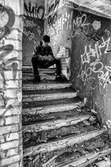 Young boy sitting on stairs in ruined building and using smarthphone