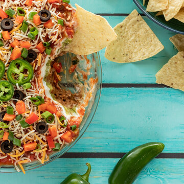 Top Down View Of A Mexican Layered Dip That Has Been Dipped Into, With Nacho Chips All Around. 