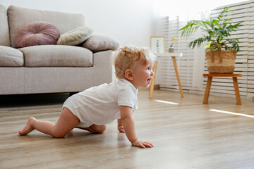 One year old child learning to crawl on the wooden floor of living room. Interior background. Adorable blonde little girl in pink crawlers at home. Close up, copy space for text. - obrazy, fototapety, plakaty