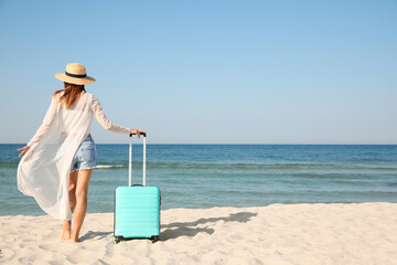 Fototapeta na wymiar Woman with suitcase on sandy beach near sea, back view