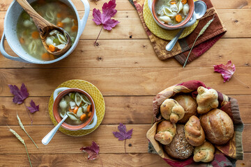 Top down view of bowls of turkey soup, served with fresh rolls, and copy space in the middle.