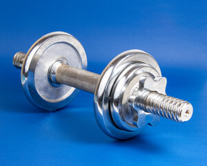 Stainless metal dumbbell on dark blue background with copyspace for text