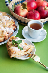 Apple homemade pie with red apples and vase of flowers on green background