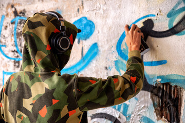 Young graffiti artist in hoodie spraying the wall.