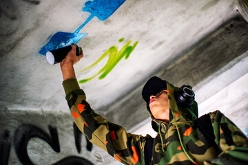 Boy in a hood spraying the wall. Graffiti concept
