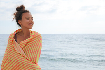 Beautiful African American woman with beach towel near sea