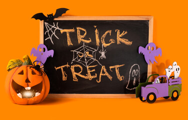 Happy halloween holiday concept. Jack o lantern, handmade paper decorations, ghost in car, bat, spider, trick or treat text on chalkboard frame on orange background. Halloween festival, greeting card