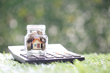 Estate tax,Model house and gold coin money in the glass bottle with calculator on natural green background,Business investment and Property tax concept