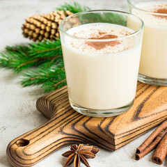 Two glasses of egg-nog and Christmas decorations on grey background