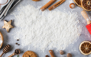  Christmas background with flour on a gray background surrounded by spices, rolling pin and cookies.