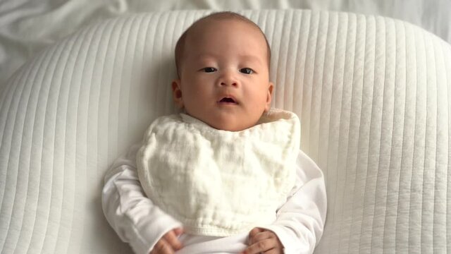 Newborn Asian infant on white cushion chatting with her mom