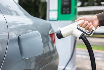 Ev car Electric car charging on parking lot. Male hand holding power cable supply plugged at Electric car charging station. Eco-friendly alternative energy. Future technology battery vehicle.
