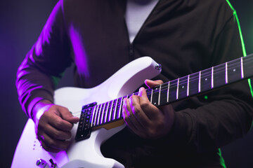 Close up hands young man rocker playing electric guitar on stage live in concert. With neon light....