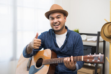 Obraz premium Lifestyle concept. Young asian musician playing guitar in living room at home on this weekend. Relaxing with song and music. Asian man having fun playing acoustic guitar