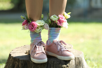 Woman standing on wooden stump outdoors with flowers in socks, closeup