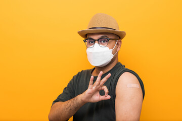 Vaccinated asian man with hat showing arm after coronavirus Vaccination isolated yellow Background....