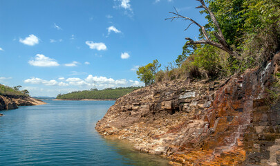 Fototapeta na wymiar Rocky walls, with vegetation on top, of the canyons of the huge lake of the Furnas dam, blue sky with clouds, Capitolio, Minas Gerais, Brazil