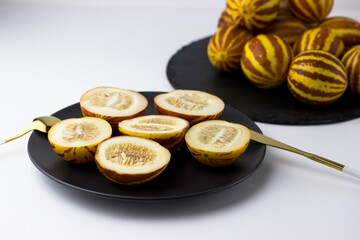 Vietnamese melon close up. Whole and cut gourmet miniature tropical fruit and knife on a black plate. Selective focus