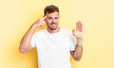 young handsome man feeling confused and puzzled, showing you are insane. hand bandage concept