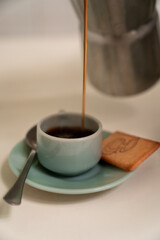 teapot pouring coffee in a cup ready to be served with a spoon and a cookie