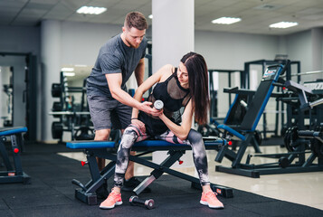 Fototapeta na wymiar Sport, bodybuilding, lifestyle and people concept. Young man and woman with barbell flexing muscles and making shoulder press squat in gym. Trainer and fitness girl are having workout at gym