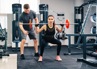 Fototapeta na wymiar Sport, bodybuilding, lifestyle and people concept. Young man and woman with barbell flexing muscles and making shoulder press squat in gym. Trainer and fitness girl are having workout at gym