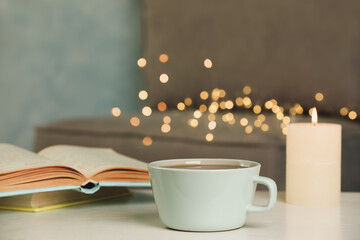 Cup of tasty freshly brewed tea, burning candle and open book on table